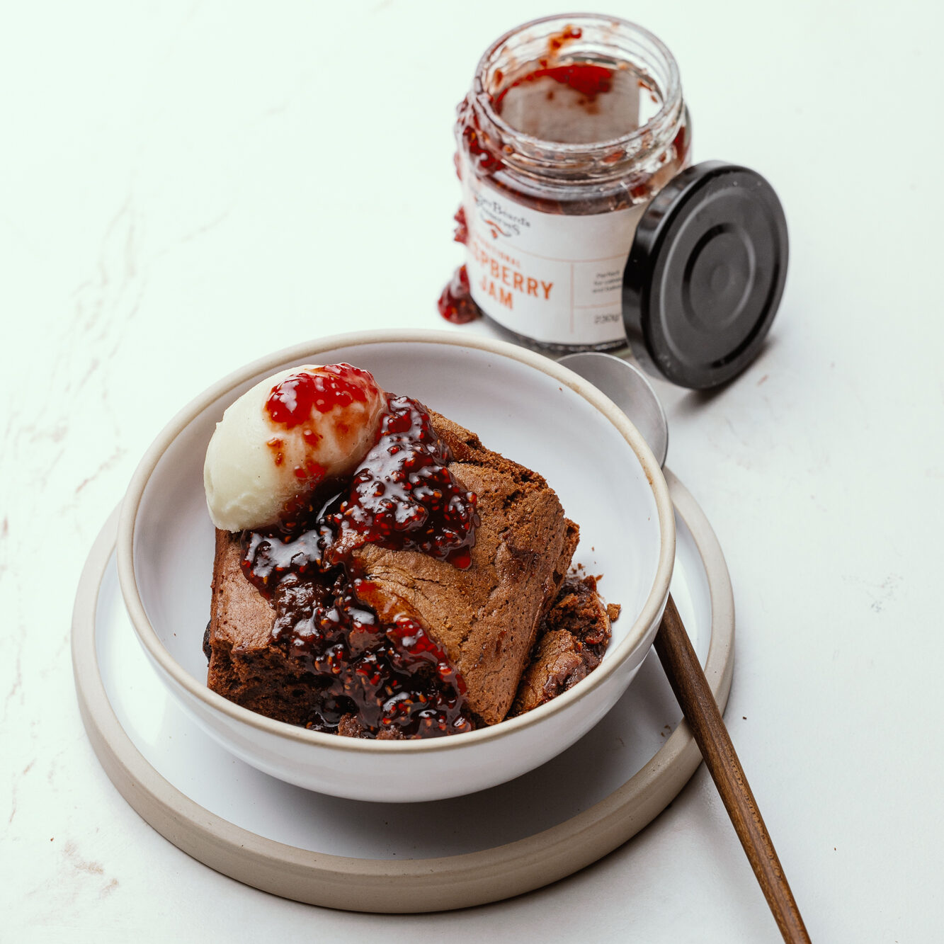 Chocolate brownie in a bowl with a jar of Raspberry Jam next to it.